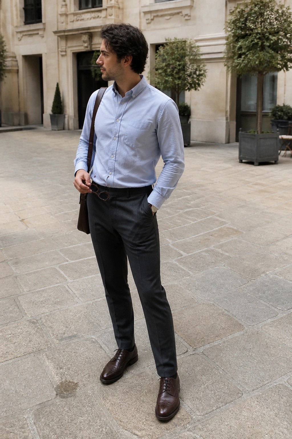 Man in light blue shirt and dark pants with leather bag in courtyard.