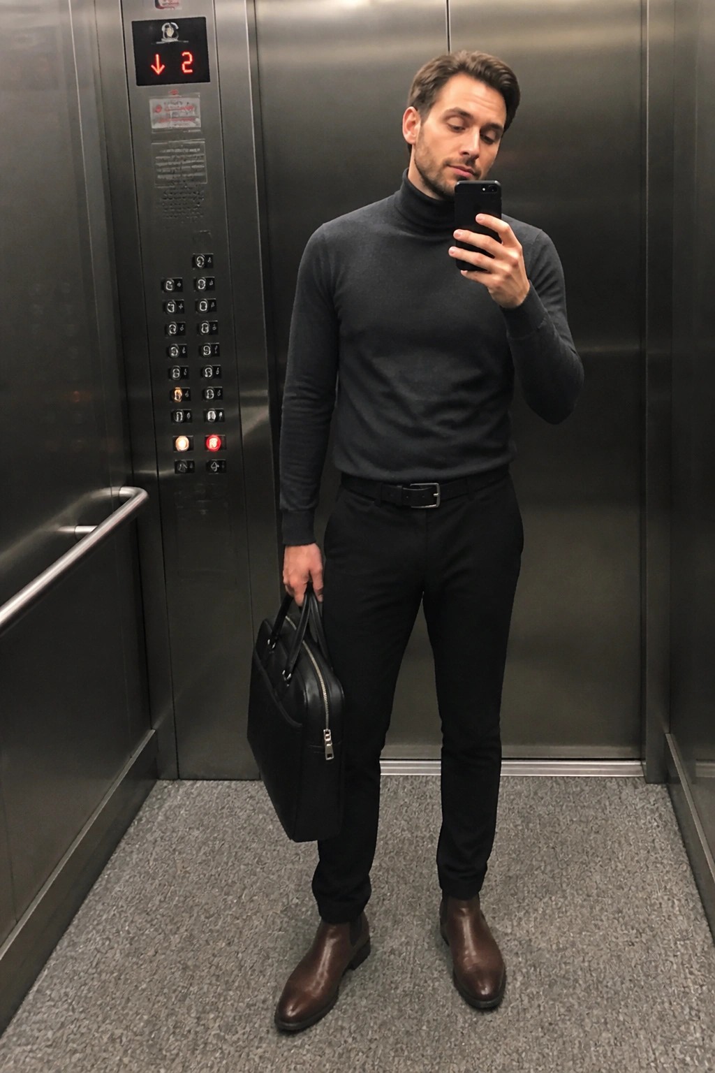 Man in gray turtleneck holding phone and briefcase in elevator