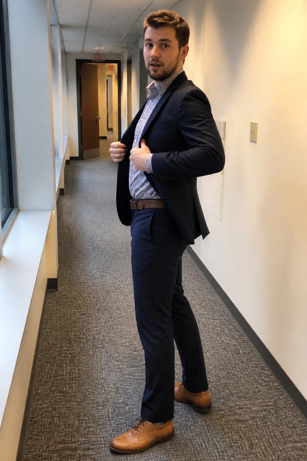 Man in navy suit adjusting jacket in office hallway