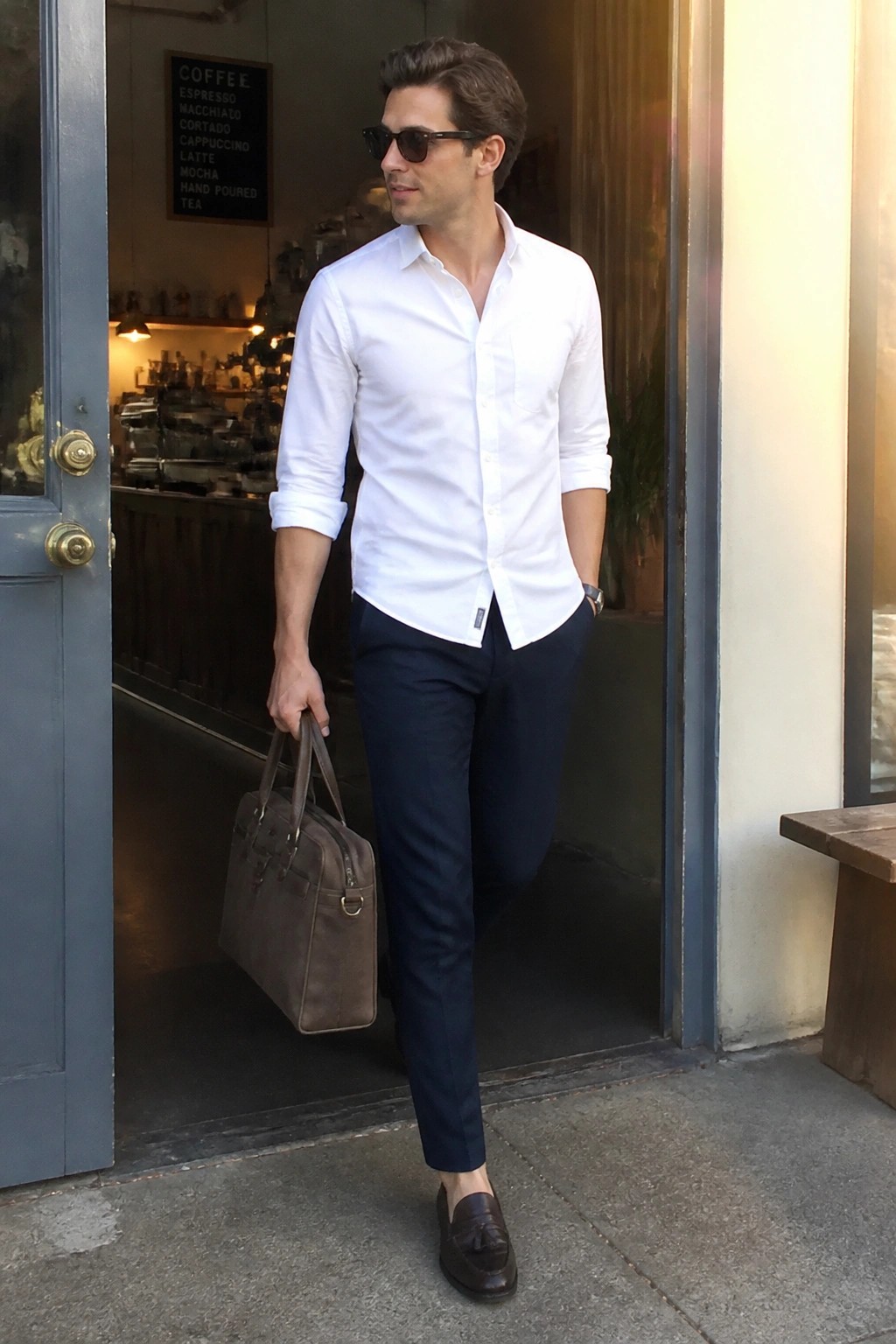 Man in white shirt and navy pants holding brown bag at cafe entrance