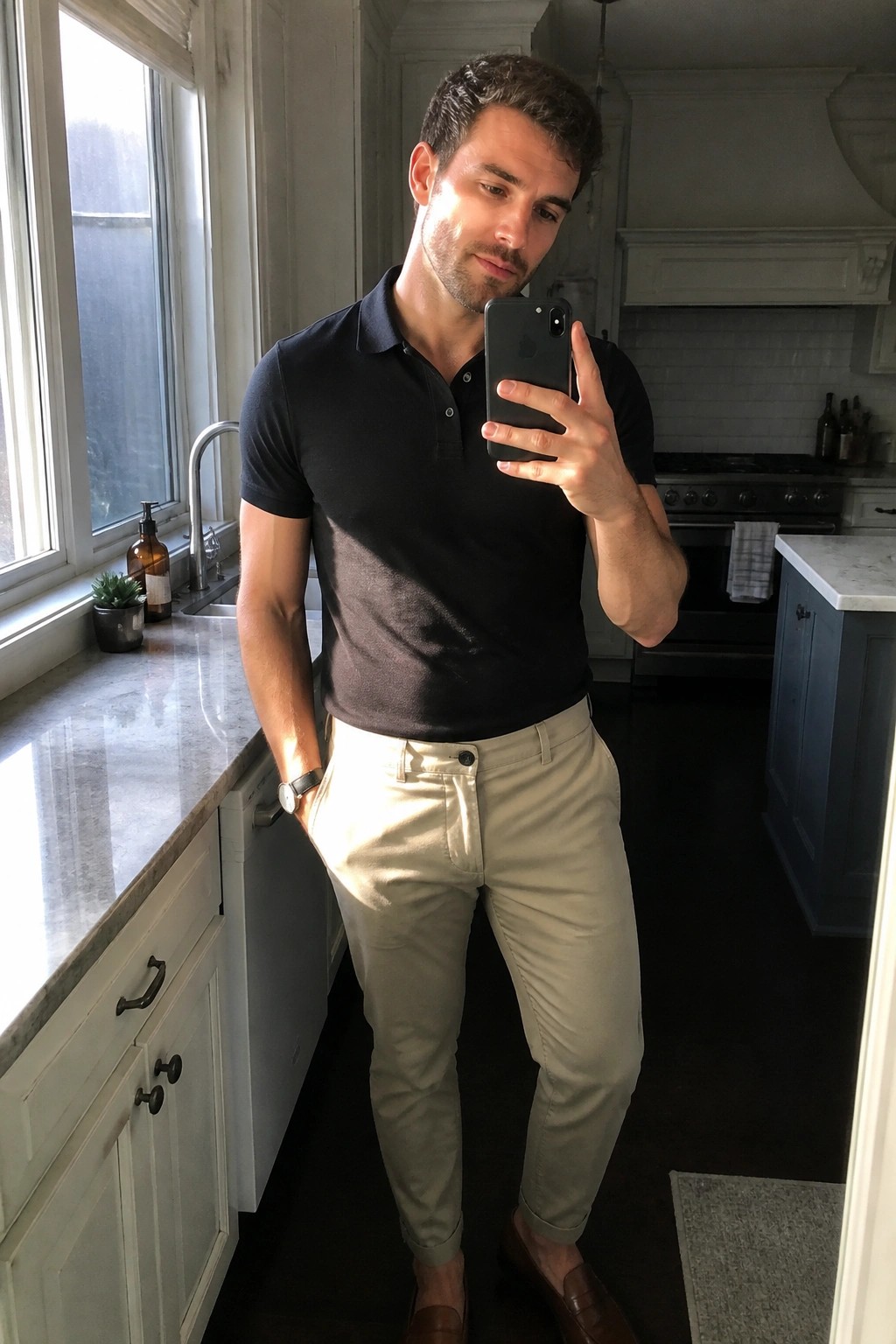 Man in black polo shirt and khaki pants taking selfie in kitchen
