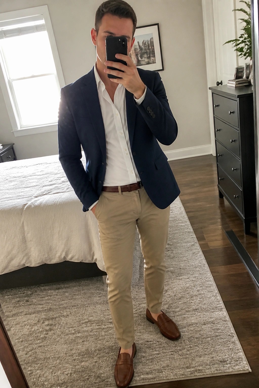 Man in navy blazer and khakis taking mirror selfie with phone