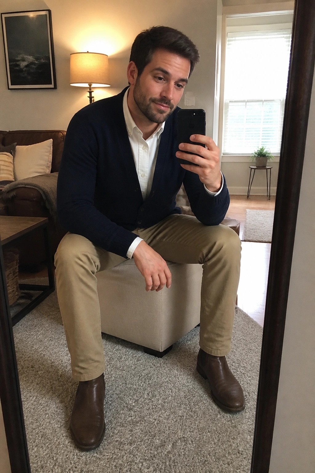Man in navy cardigan and khaki pants taking mirror selfie on smartphone