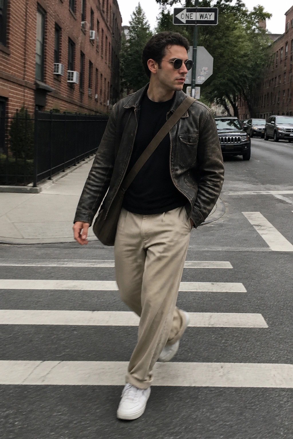Man in leather jacket and beige pants crossing urban crosswalk