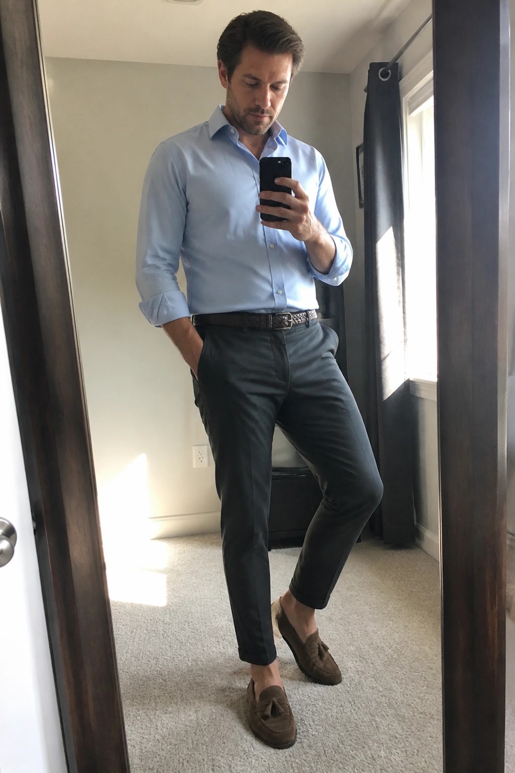 Man in light blue shirt and dark pants taking mirror selfie with phone