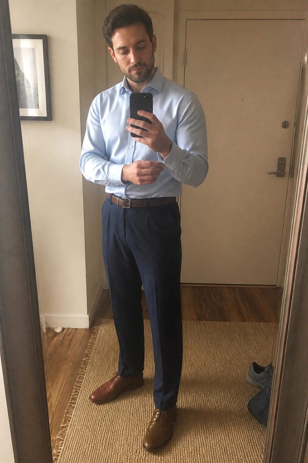Man in light blue shirt and navy pants taking mirror selfie with phone