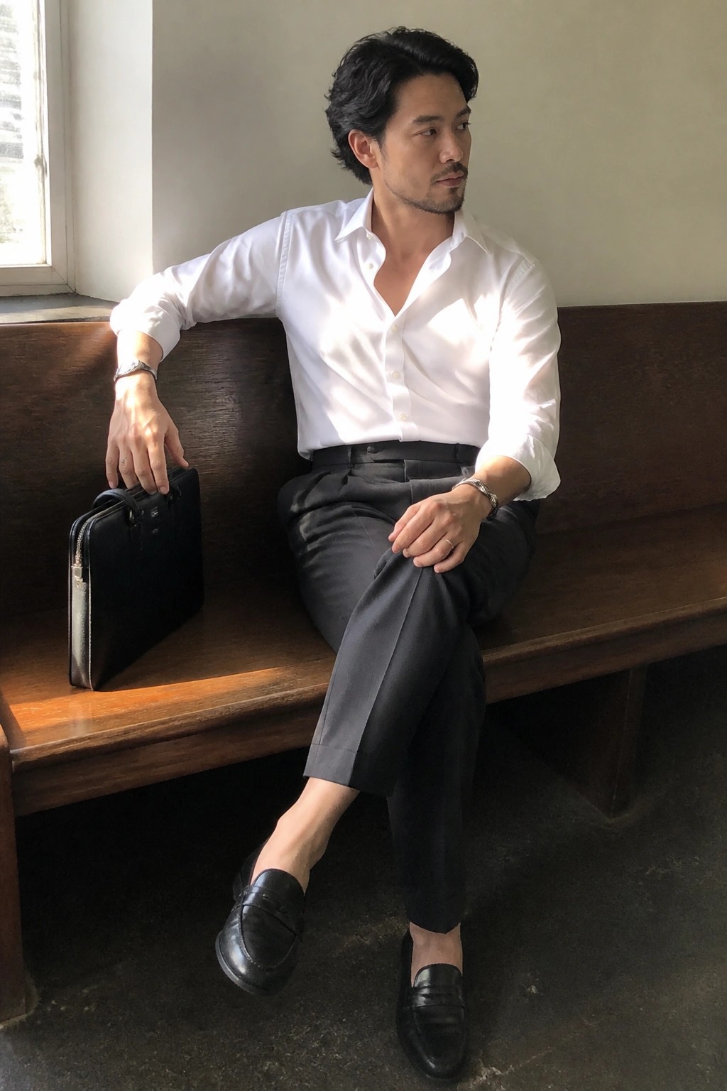 Man in white shirt and black trousers seated on wooden bench holding briefcase