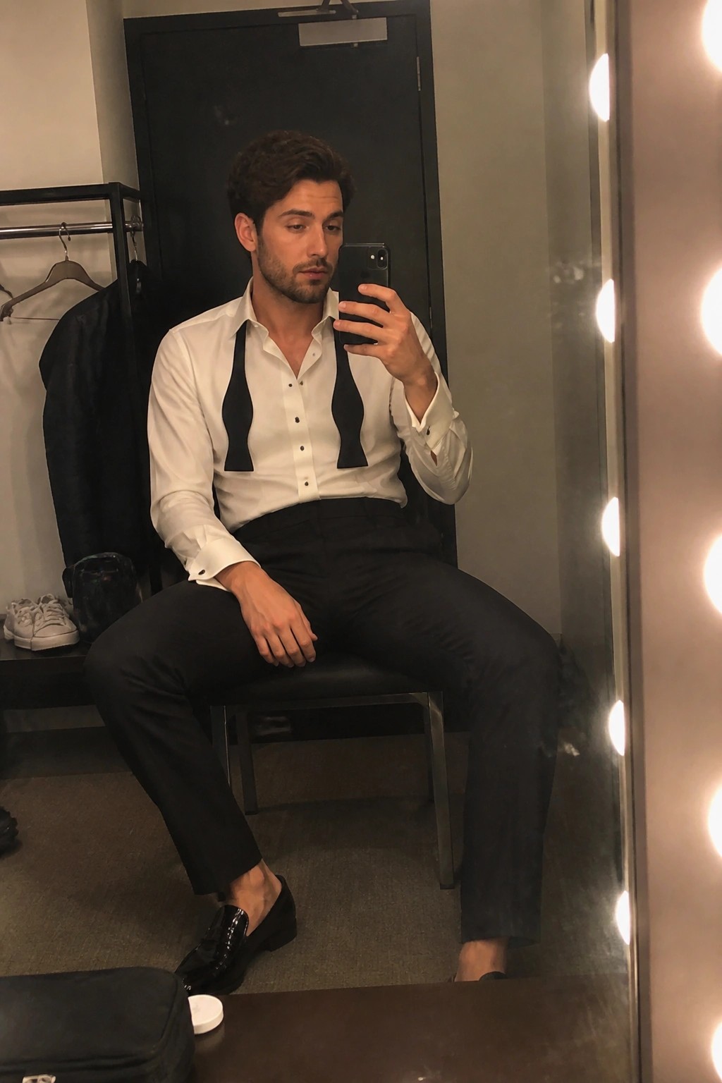 Man in white shirt with black bows takes mirror selfie in dressing room