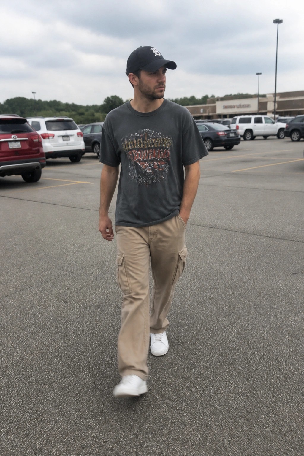 Man in black cap, gray graphic tee, beige cargo pants in parking lot