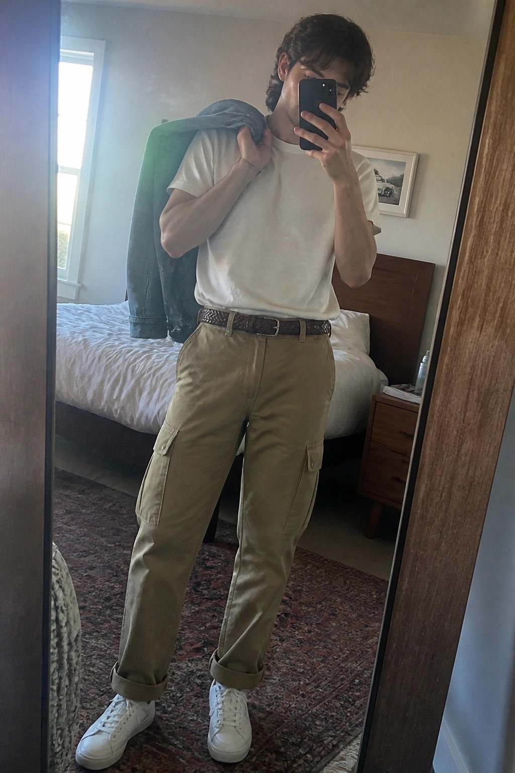 Young man in white t-shirt and khaki cargo pants holding green jacket for mirror selfie