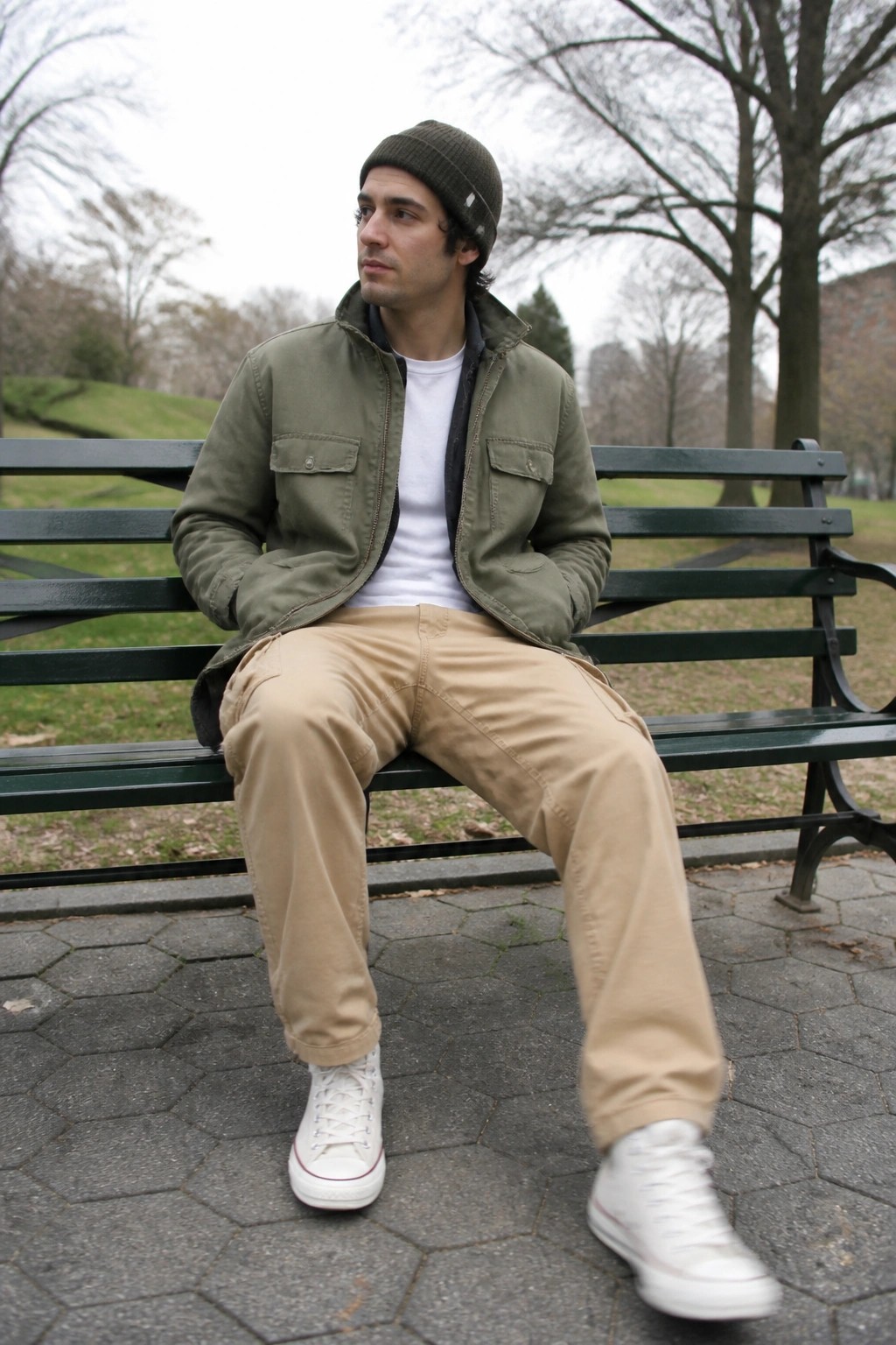 Man in green jacket and beanie sitting on park bench looking aside
