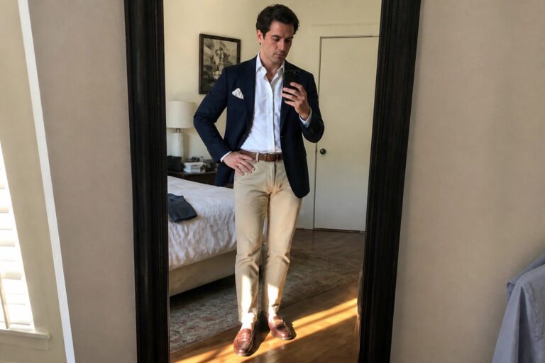 21 Sophisticated Men’s Wedding Guest Outfits Built Around Khaki Trousers and Tailored Layers Man in navy blazer and khaki pants taking smartphone mirror selfie in bedroom