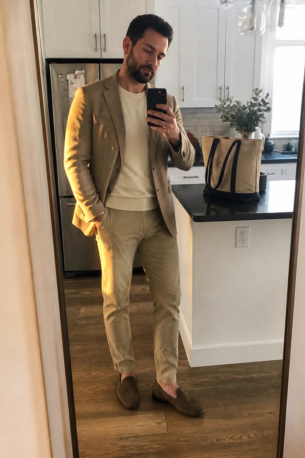 Man in tan blazer over cream sweater with matching pants in kitchen mirror selfie
