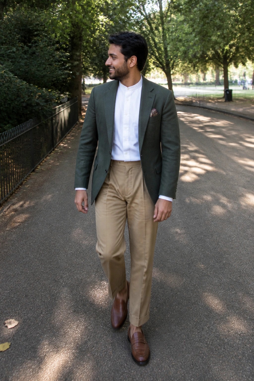 Man in green blazer, white shirt, and beige pants smiles on park path.