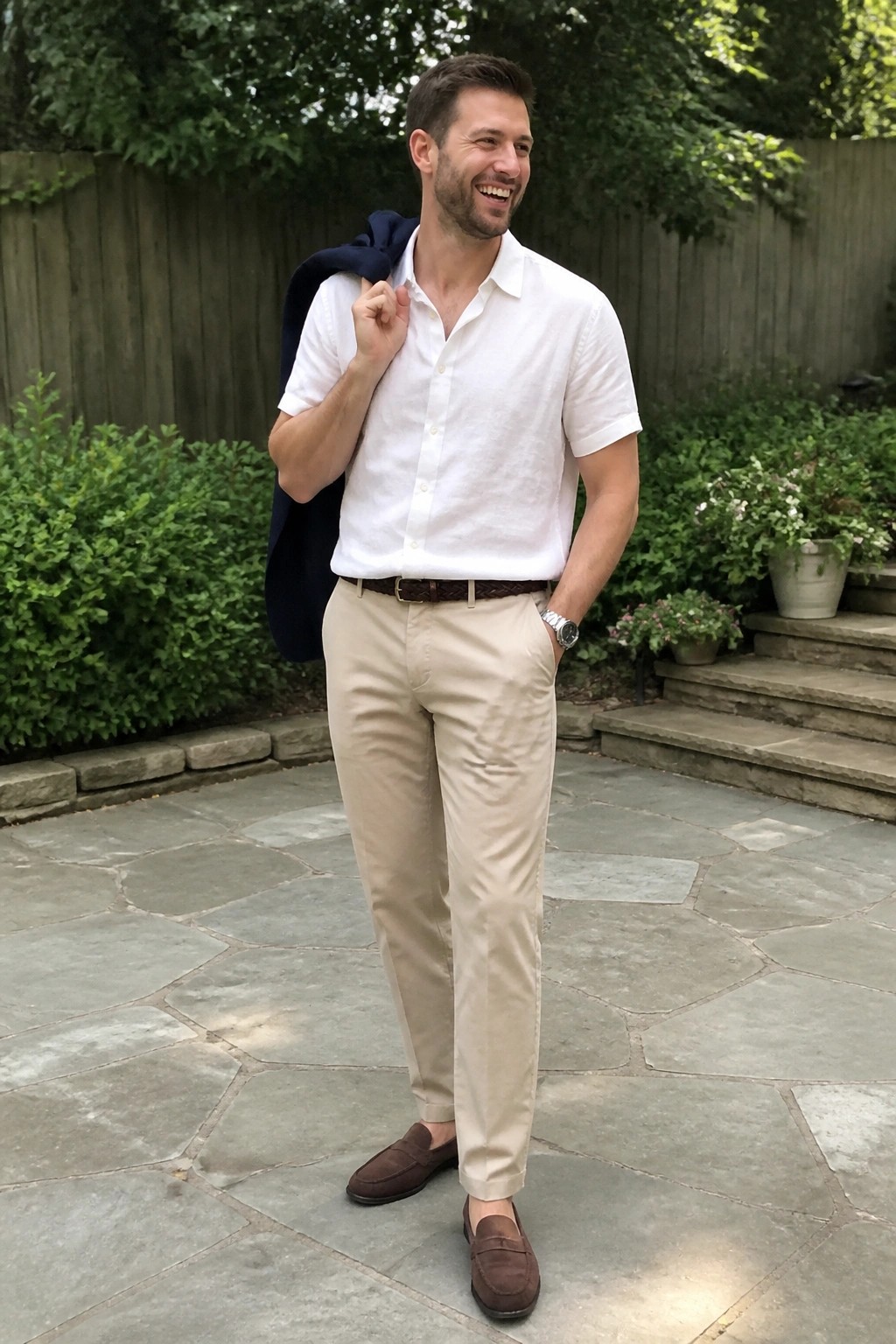 Man in white shirt and beige pants holding navy blazer on stone patio
