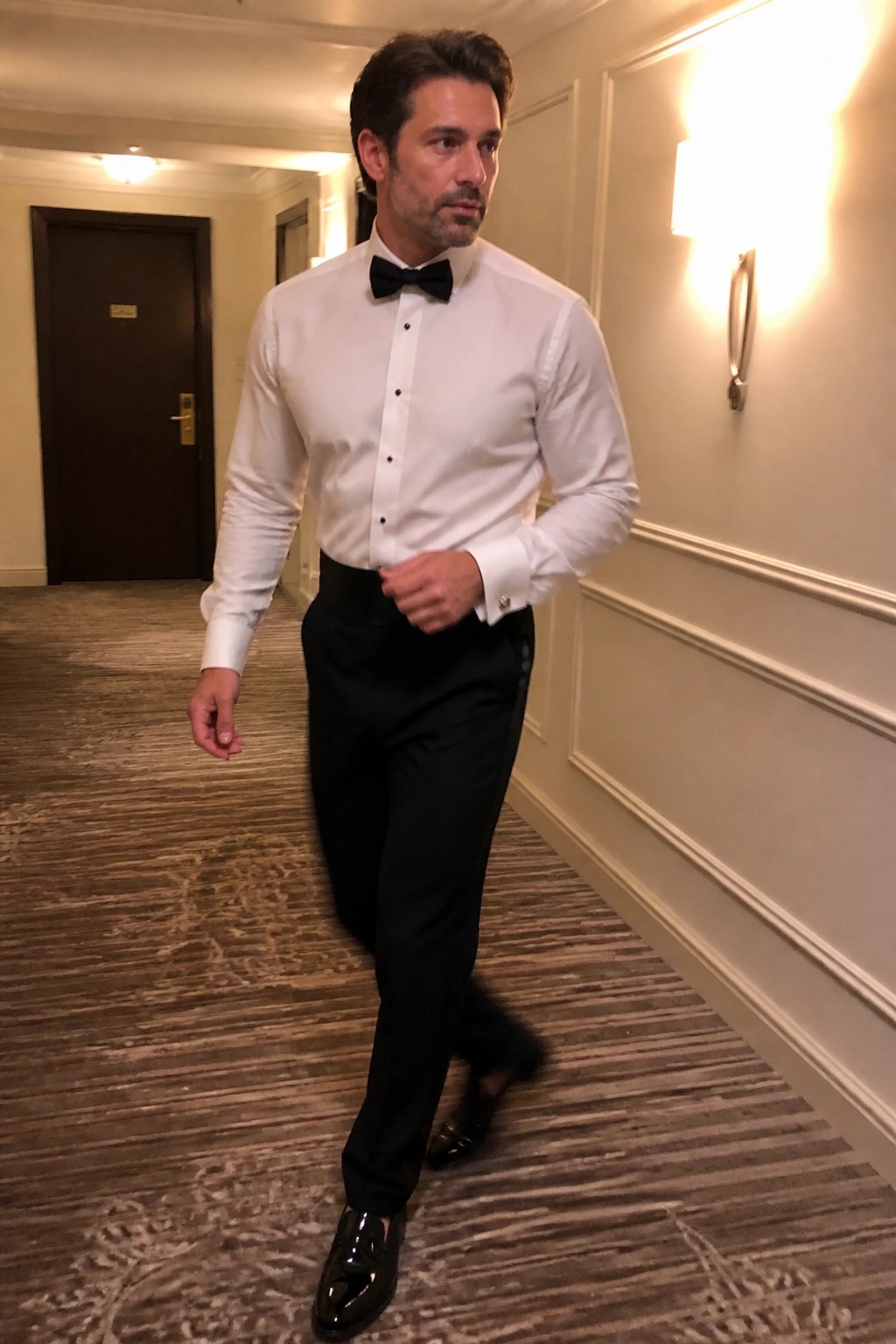 Man in white shirt and black bow tie walking in carpeted hallway