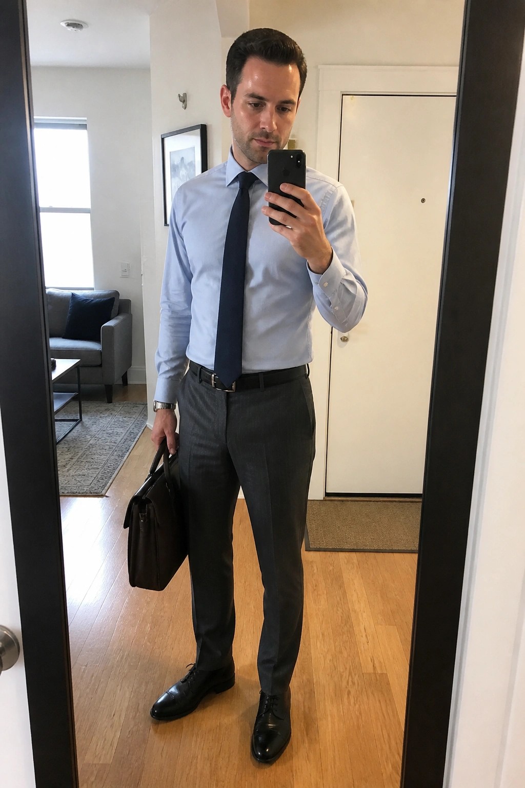 Businessman in light blue shirt and tie taking mirror selfie with briefcase.