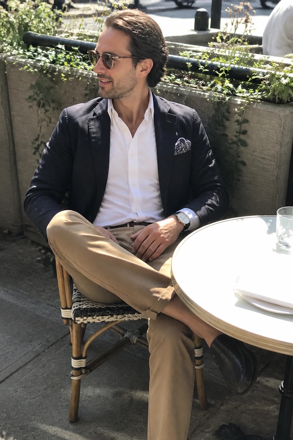 Man in navy blazer, white shirt, and beige pants at outdoor cafe table