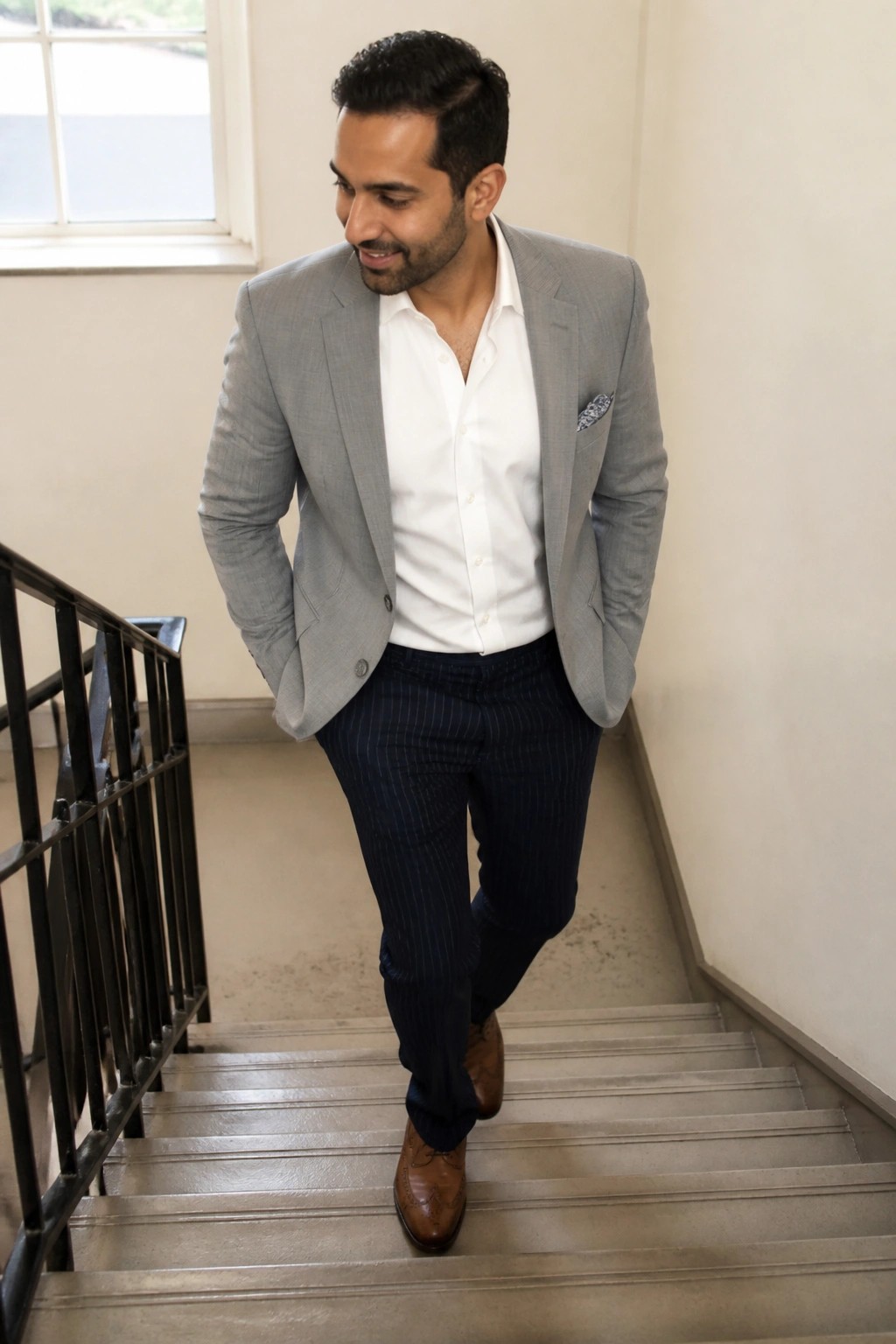 Man in gray blazer and pinstripe pants walking down stairs, hands in pockets