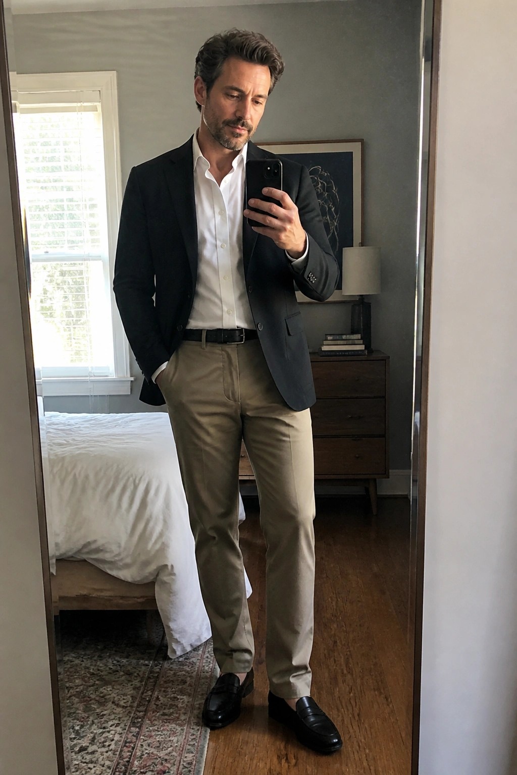 Man in black blazer, white shirt, and khaki pants taking mirror selfie.