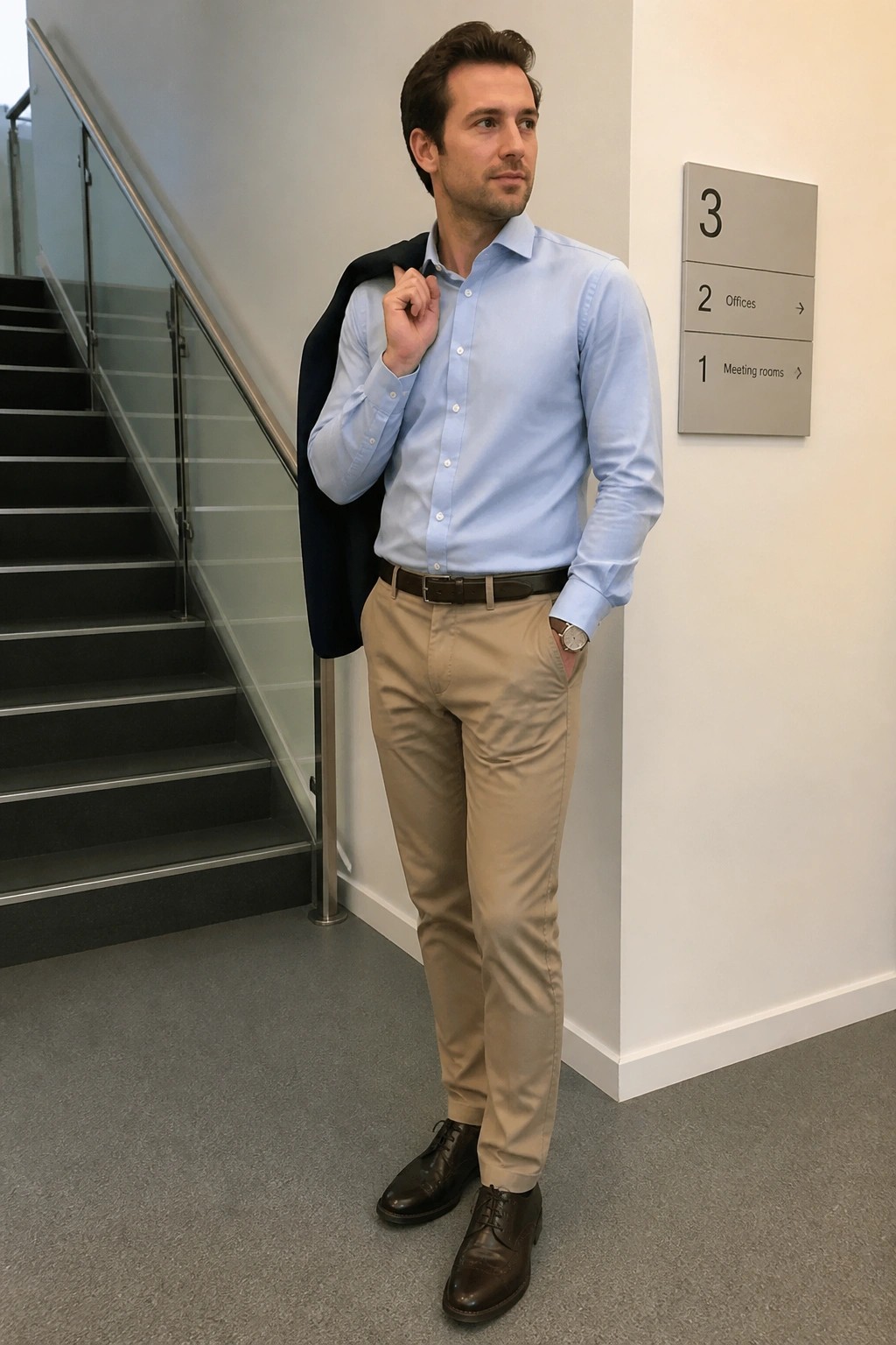 Man in light blue shirt and khakis holding navy blazer over shoulder by staircase