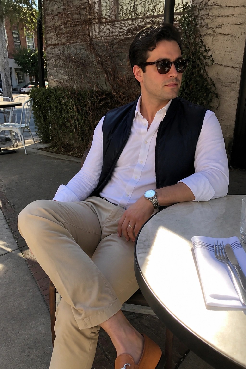 Man in white shirt and navy vest seated at outdoor cafe table