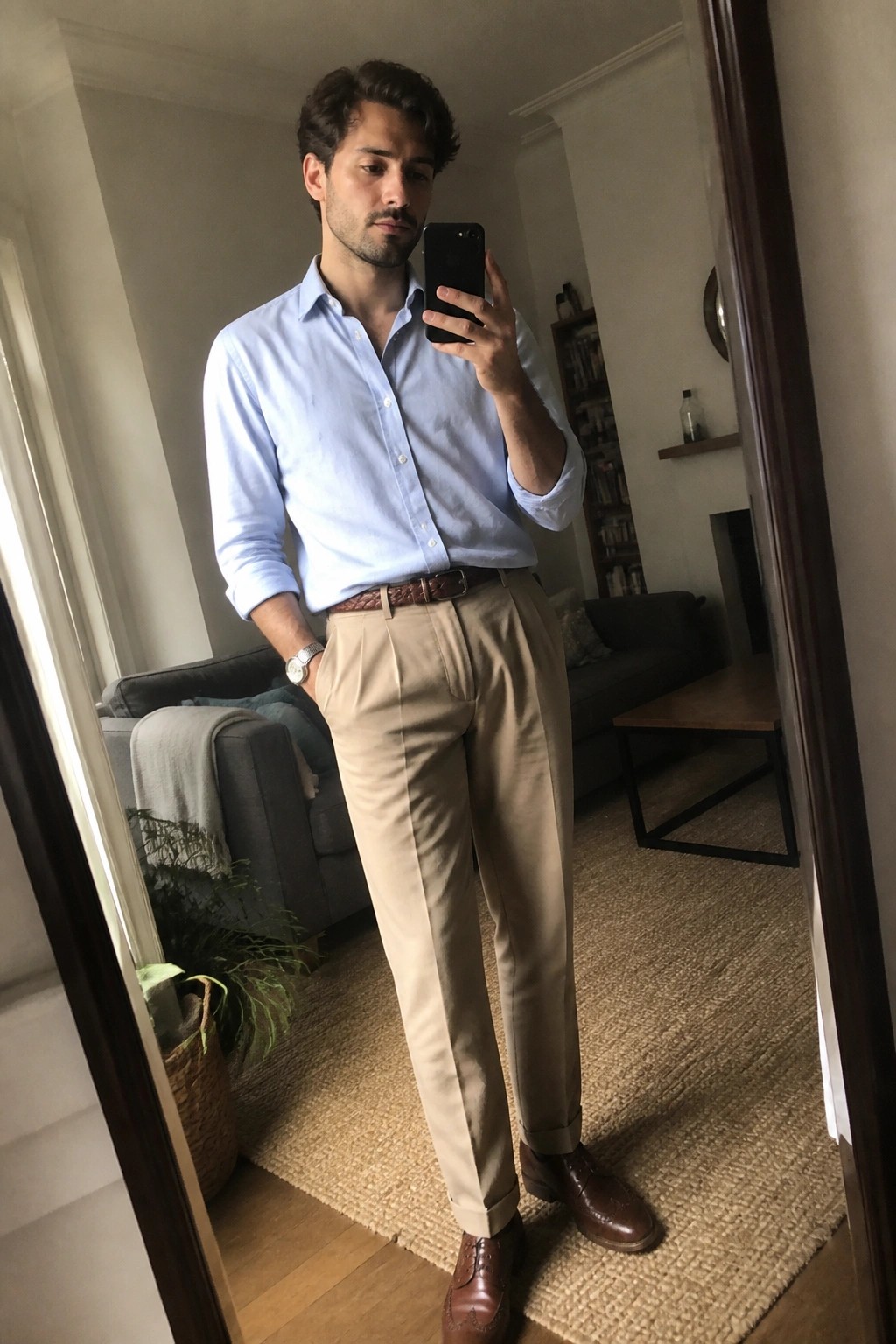 Man in light blue shirt and beige trousers taking mirror selfie in living room