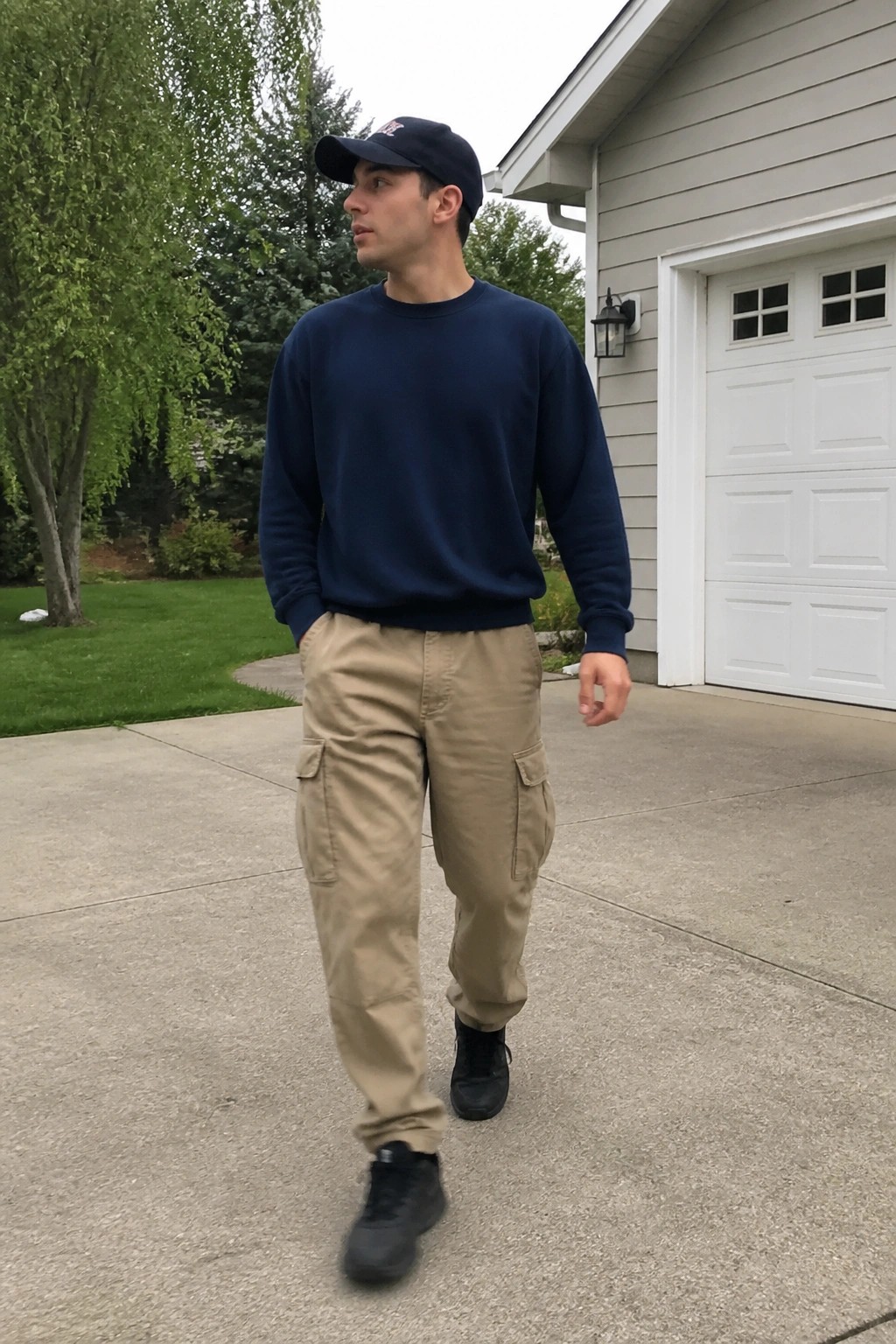 Man in navy sweatshirt, khaki cargo pants, and cap on driveway