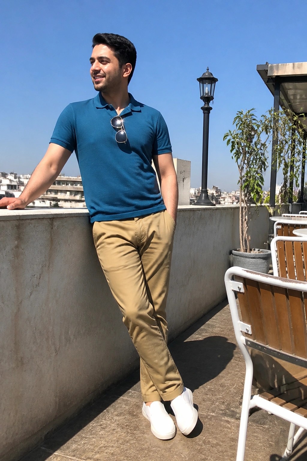 Man in blue polo shirt and khaki pants on sunny rooftop terrace.