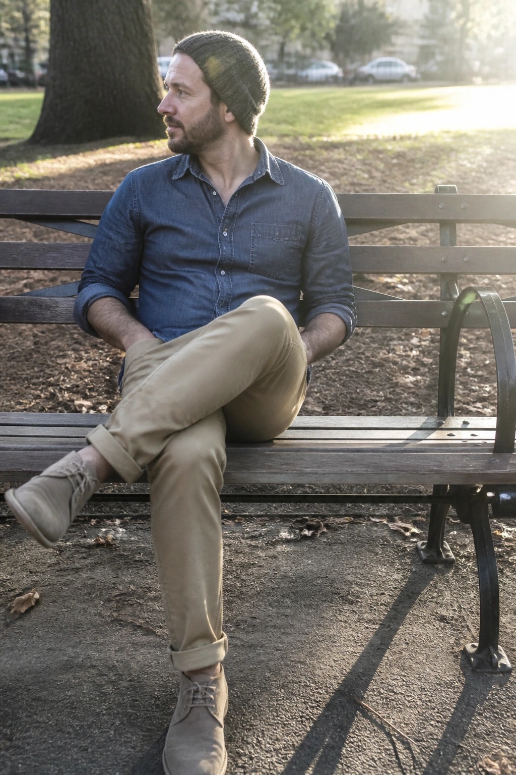 Bearded man in blue denim shirt and khaki pants on wooden park bench