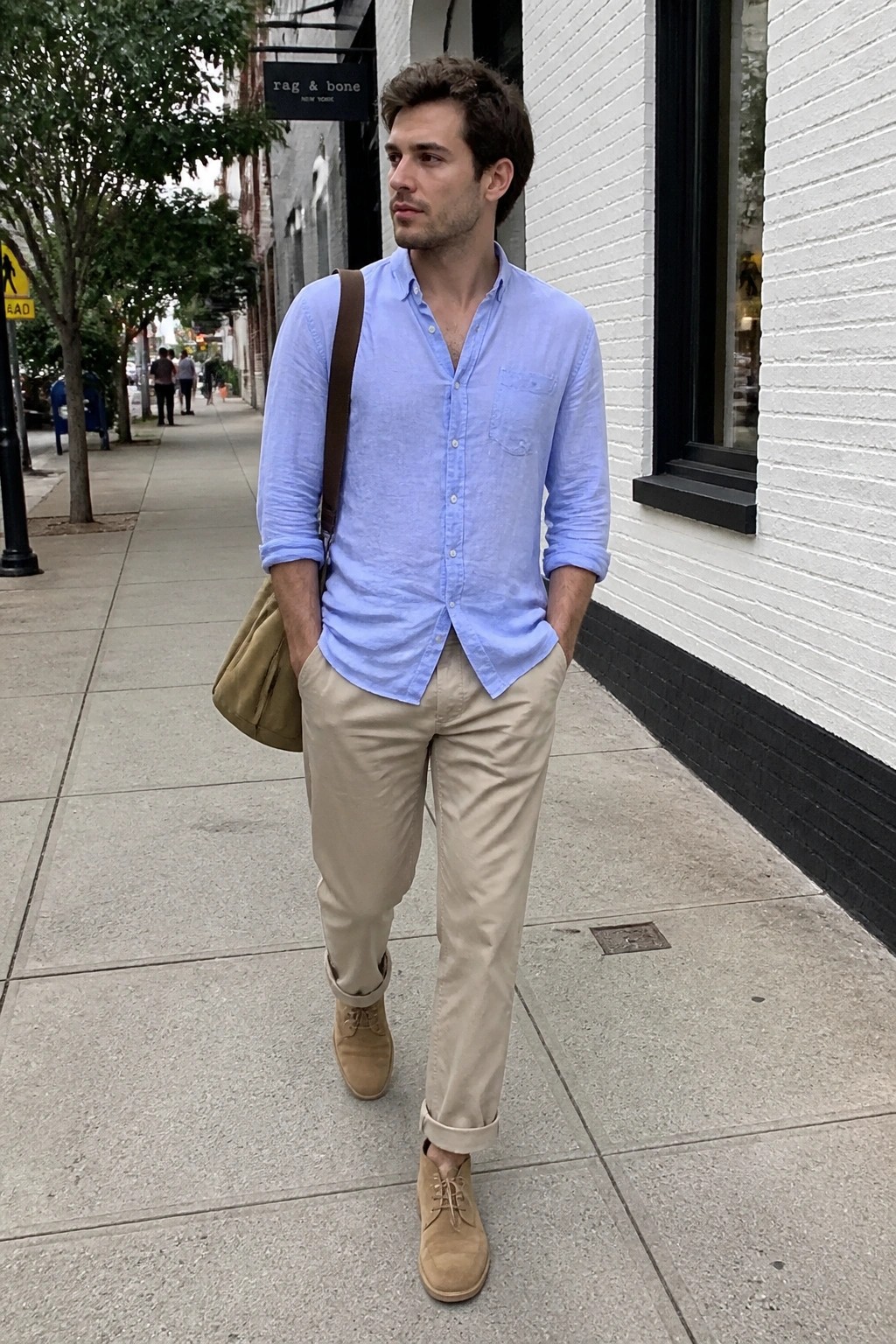 Man in light blue shirt and beige pants on city sidewalk with brown bag