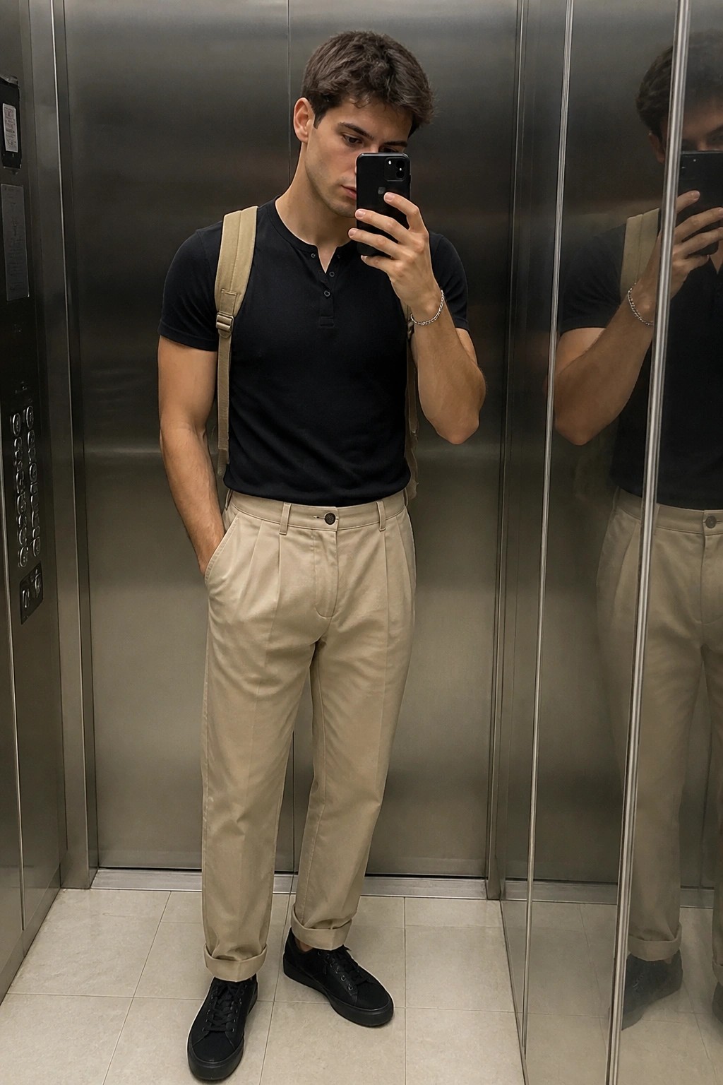 Young man in black henley and beige pants taking elevator mirror selfie