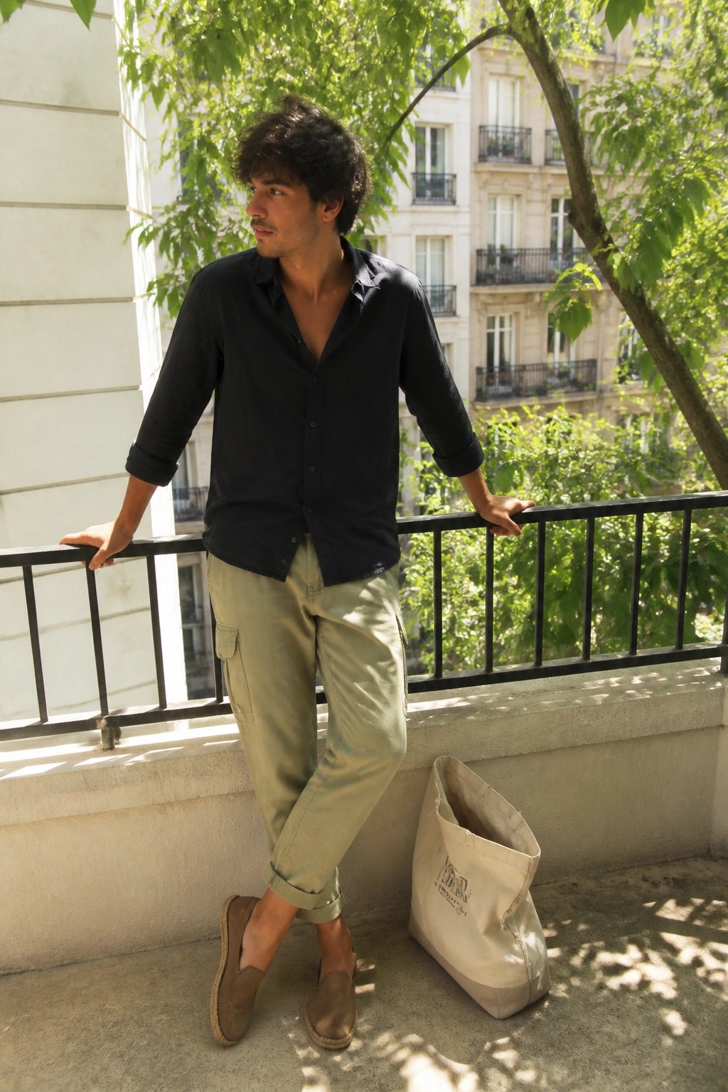 Man in navy shirt and green cargo pants on sunny balcony with tote bag