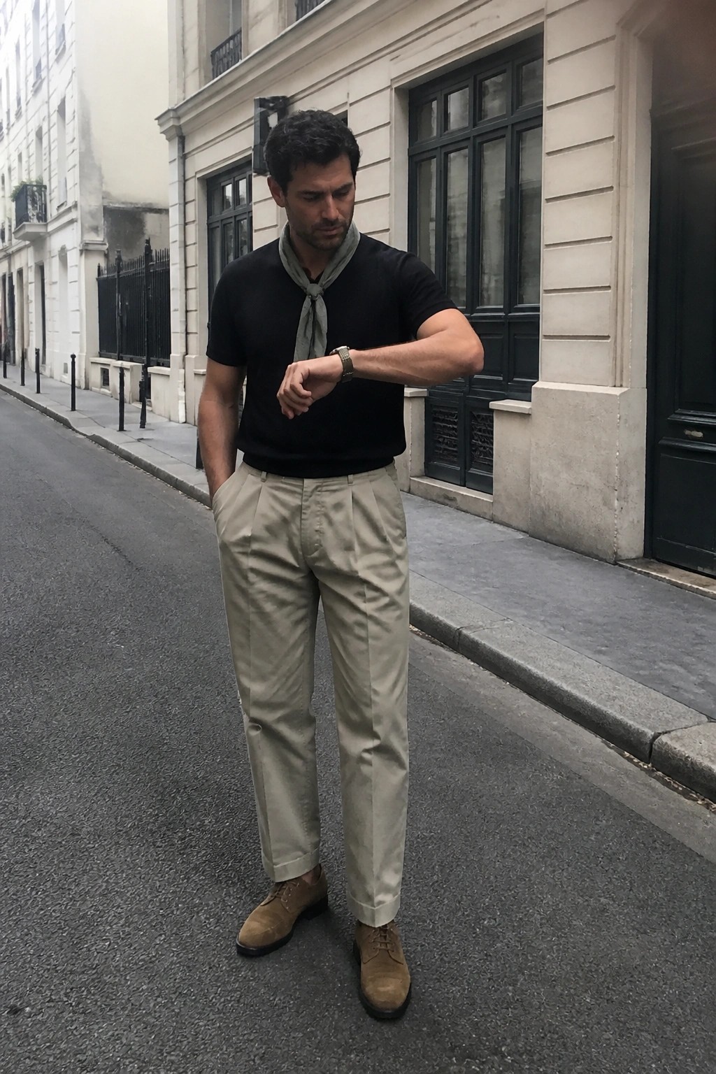 Man in black t-shirt and beige pants checking watch on city street