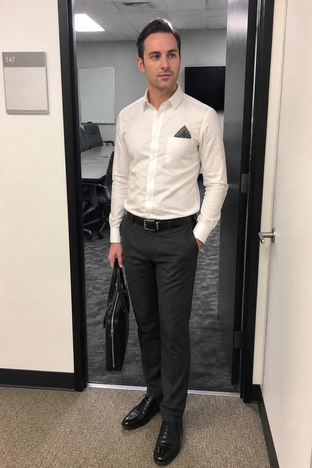 Businessman in white shirt and gray pants holding briefcase in office doorway