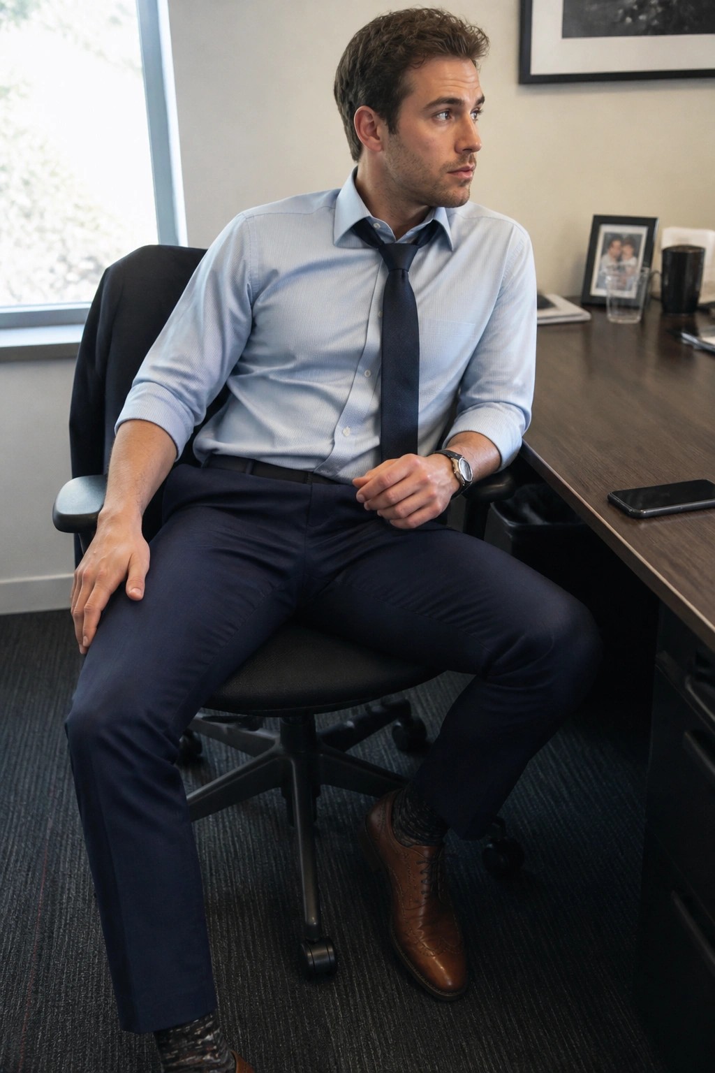 Man in light blue shirt and dark tie seated in black office chair