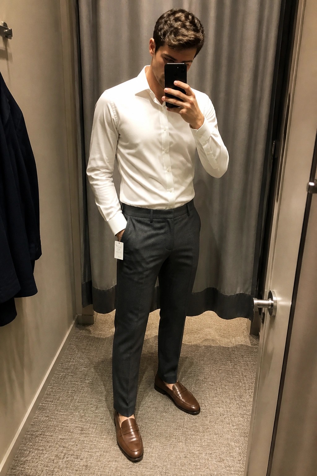 Man in white shirt and gray pants taking mirror selfie in fitting room