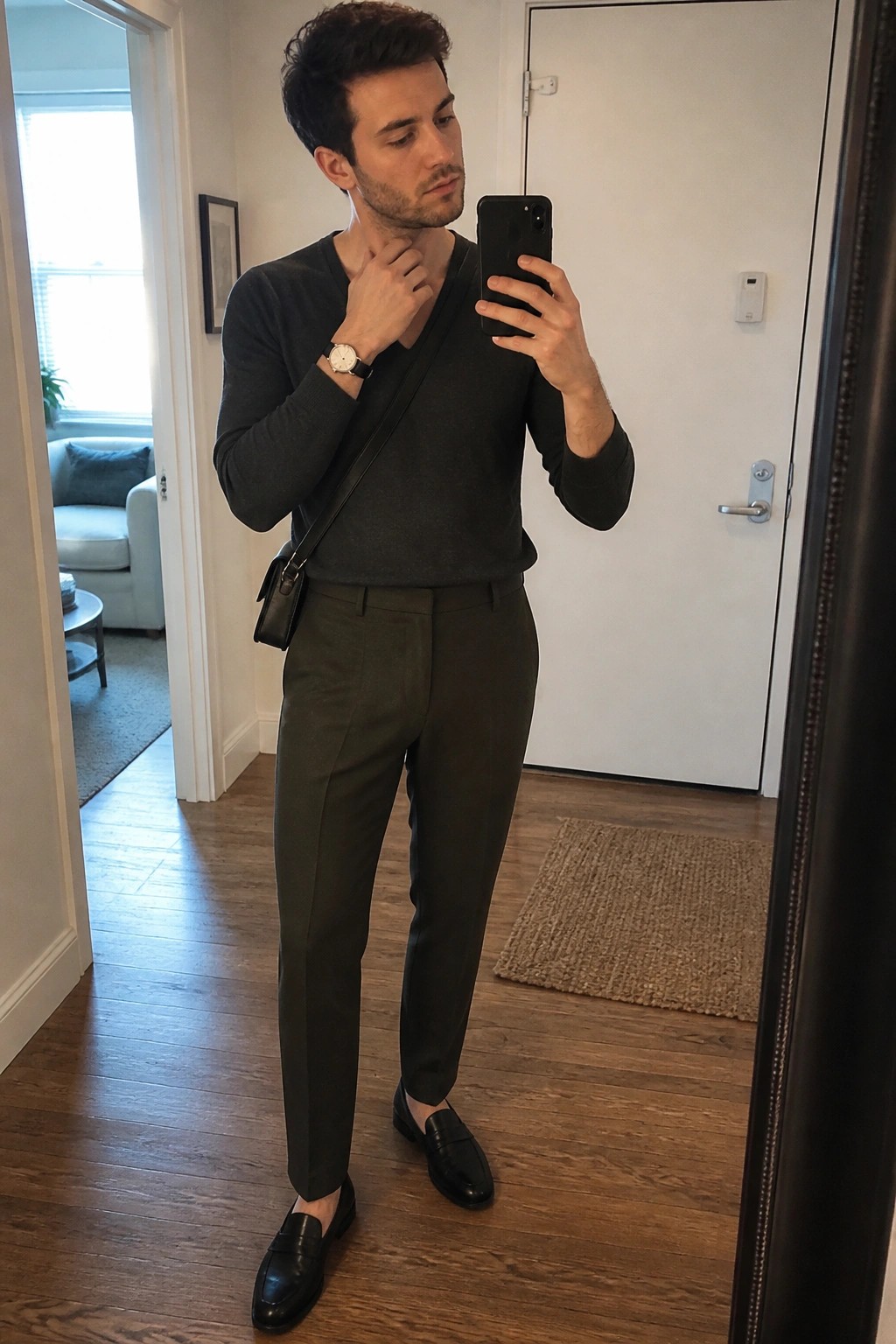 Man in dark sweater and olive trousers taking mirror selfie with phone