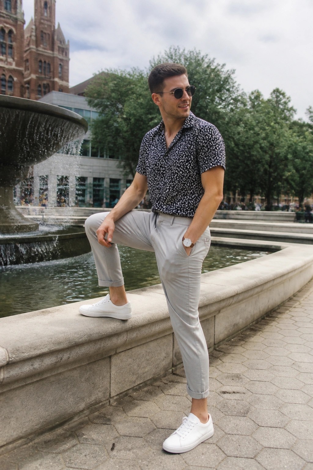 Man in patterned shirt and gray pants posing by stone fountain