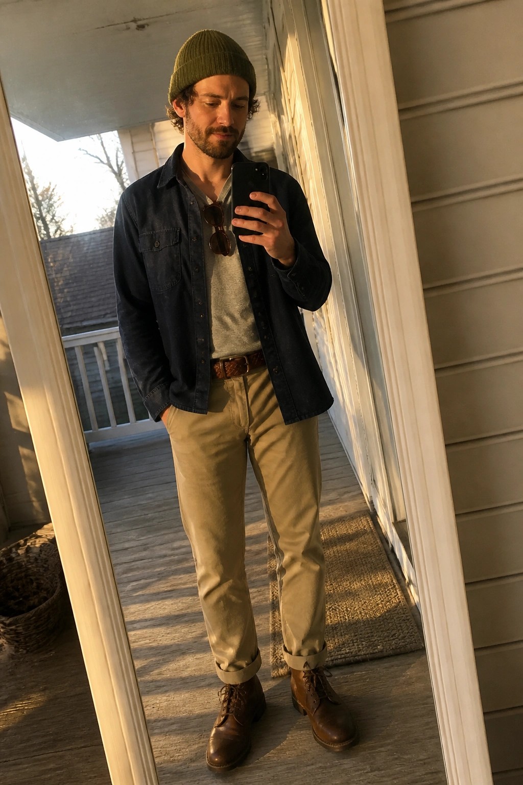 Man in green beanie and denim shirt takes mirror selfie on porch