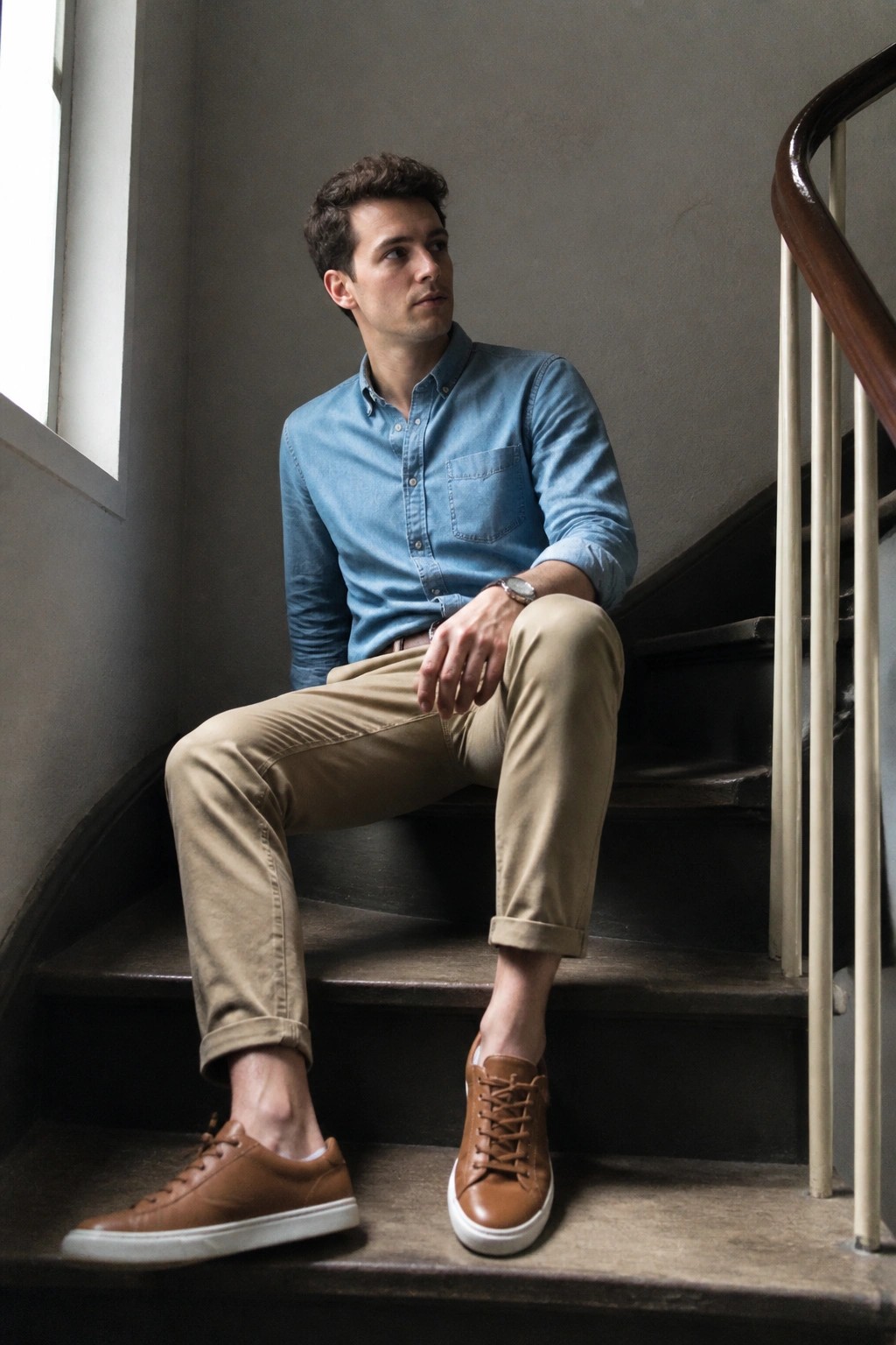Man in blue shirt and khaki pants seated on wooden staircase