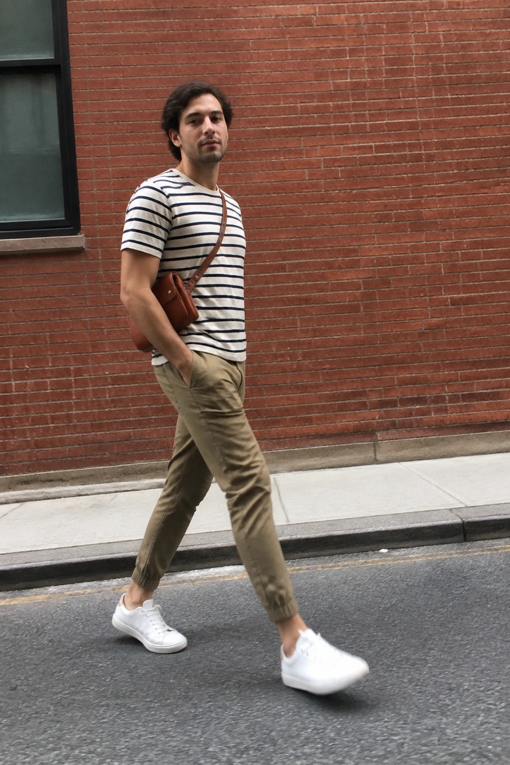 Man in striped shirt and khaki pants walks on street with brown bag