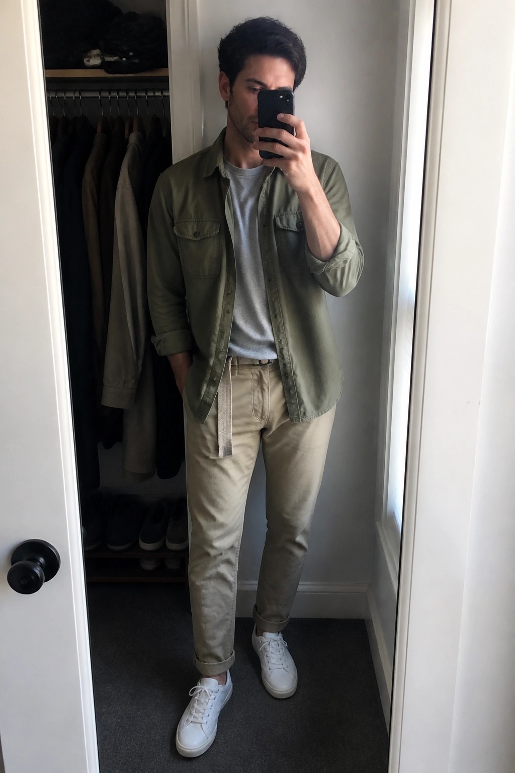 Man taking mirror selfie in green shirt, khaki pants, and white sneakers
