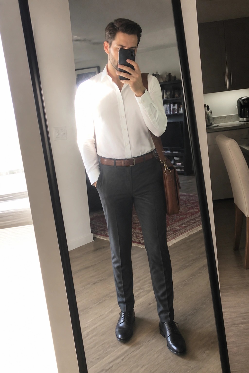 Man in white shirt and gray pants taking mirror selfie with leather bag