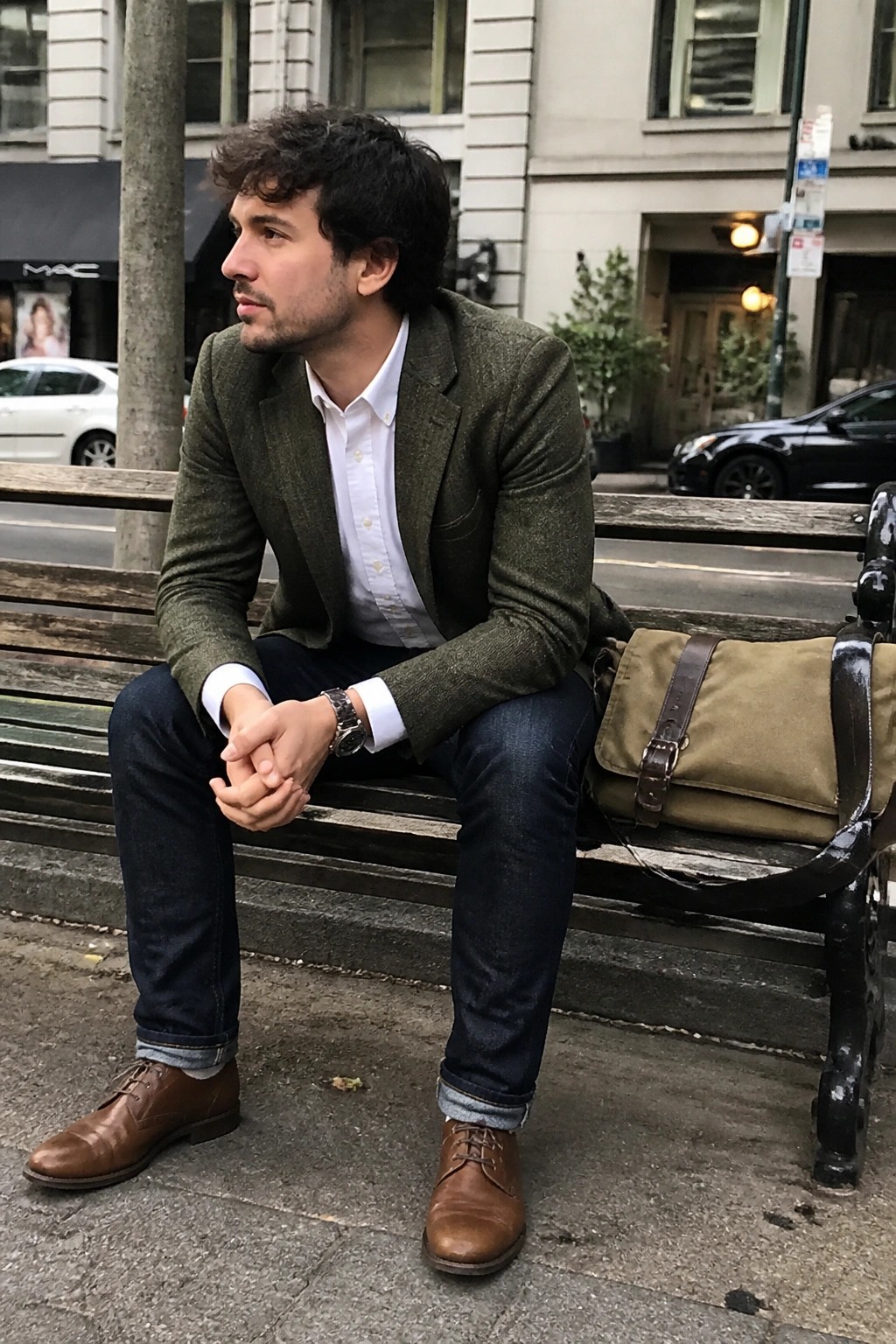 Man in green blazer and jeans sits on bench with canvas messenger bag