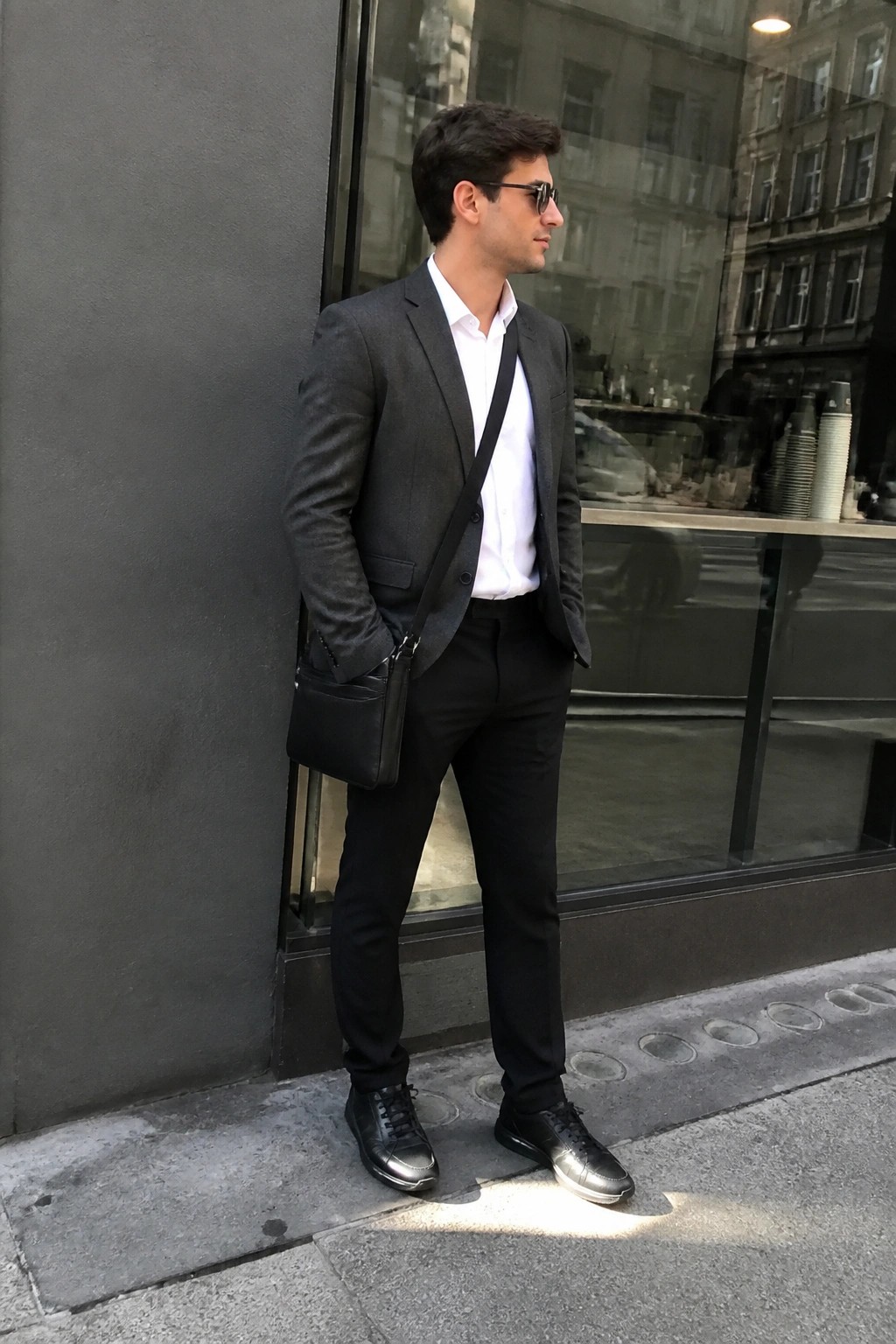 Man in gray suit jacket, white shirt, black pants with crossbody bag on sidewalk