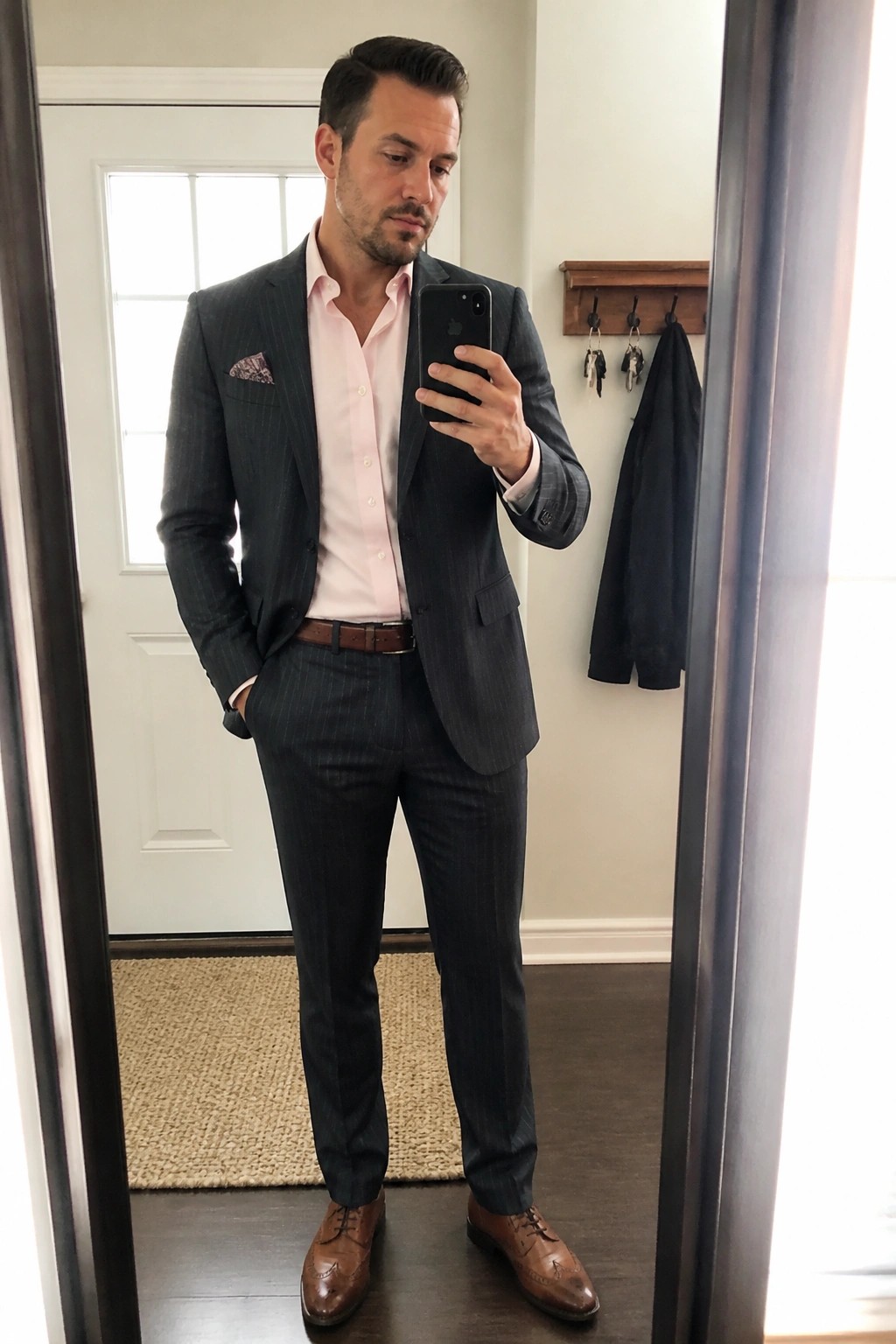 Man in dark pinstripe suit with pink shirt taking mirror selfie holding phone