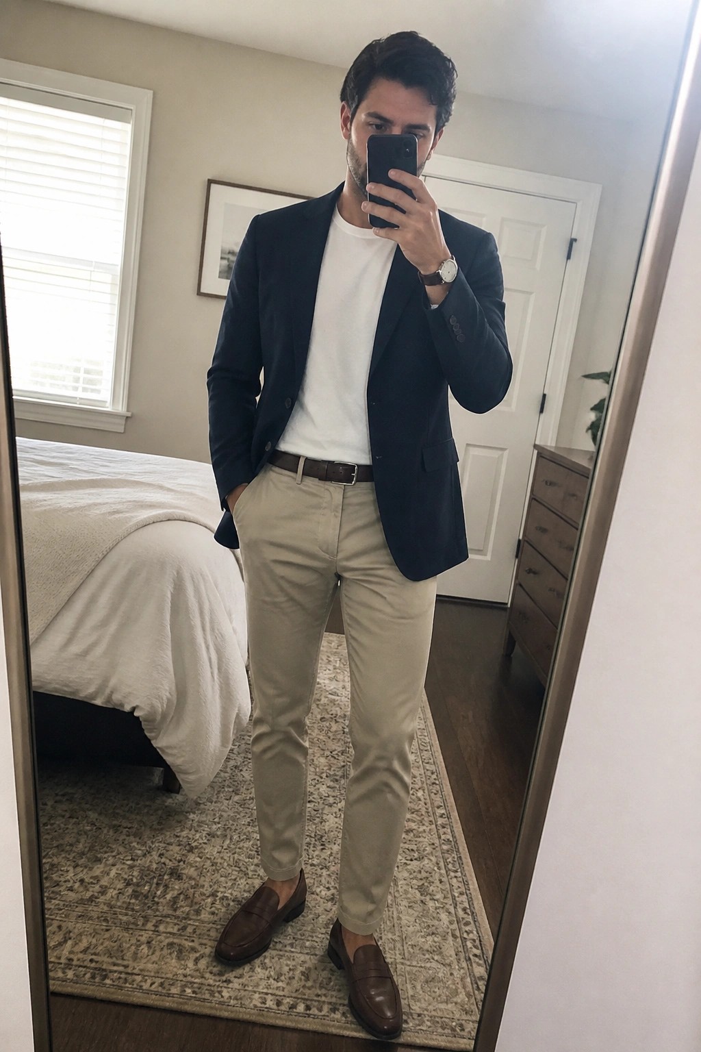 Man in navy blazer, white tee, khaki pants, and brown loafers taking mirror selfie