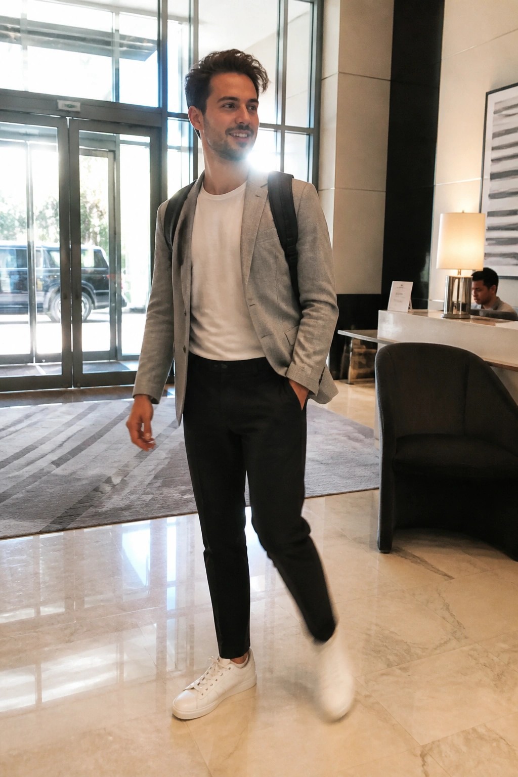 Man in gray blazer with backpack walking across marble hotel lobby