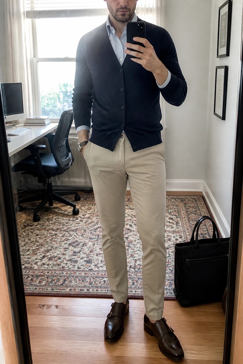 Man in navy cardigan, light shirt, beige pants, and brown monk shoes taking selfie
